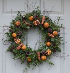 a wreath with oranges and pine cones hanging on the front door to decorate it