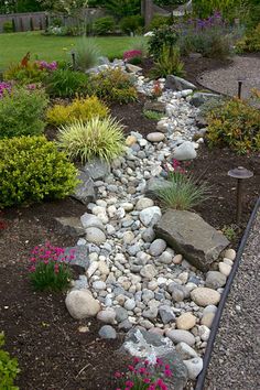 a garden with rocks and flowers in the center, along side a path that leads to a house