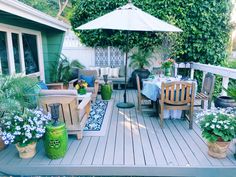 a deck with chairs, tables and an umbrella over it is surrounded by potted plants