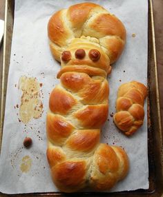 bread shaped like a bear laying on top of a sheet of wax paper next to some croissants