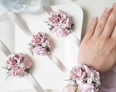 a woman's hand with three pink flowers on her wrist and two white ribbons