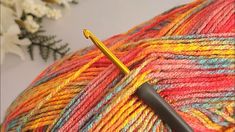 a ball of yarn with a crochet hook in the foreground and flowers in the background