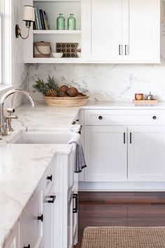 a kitchen with white cabinets and marble counter tops