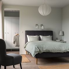 a bed sitting in a bedroom next to a chair and lamp on top of a hard wood floor