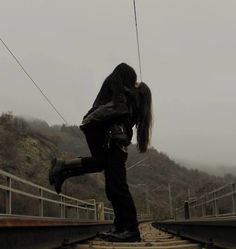 a woman with long hair standing on train tracks in the rain, holding onto wires