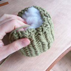 a hand holding a green crochet pot holder with cotton in it and a wool ball inside