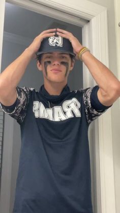 a young man wearing a baseball cap and holding his hands up to his head while standing in front of a door