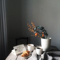 two cups of coffee and a croissant on a table next to a book