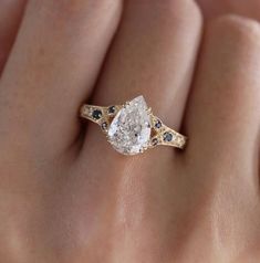 a woman's hand holding an engagement ring with a pear shaped diamond in the center