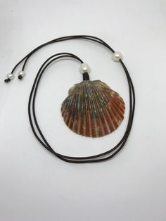 a necklace with a seashell and pearls hanging from it's cord on a white background