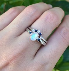 "A unique oval-shaped faceted rainbow moonstone engagement ring set accented with 2 petite genuine blue sapphires complemented with a matching contour wedding band featuring genuine blue and white sapphires handcrafted in sterling silver. Wrapped in a box ready for gift-giving.(r-egt-9) Instagram Video --------------- https://instagram.com/p/Bl3qWYXFgUA/ Can be custom made in any material and gemstones Center stone measure 7mm x 6mm Side Stone measures 2.2mm ----> Please note there is an addi Rainbow Moonstone Engagement Ring, Moonstone Engagement Ring Set, Sapphire Engagement Ring Set, Contour Wedding Band, Moonstone Engagement, Moonstone Engagement Ring, Sapphire Engagement Ring, Bridal Ring Set, Sapphire Engagement