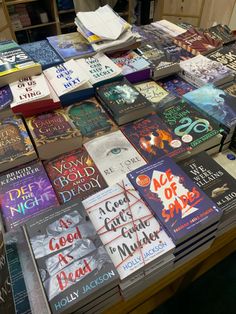 many books are stacked on top of each other in front of a wooden table full of them