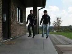 two young men walking down a sidewalk next to a brick building with grass and trees in the background