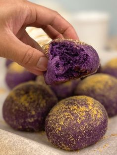 a hand holding a purple doughnut with gold sprinkles on top of it