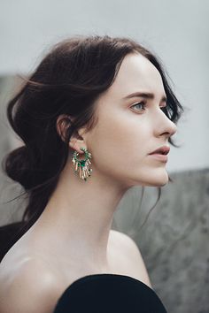 a woman in black dress wearing green and gold earring with large leaves on it