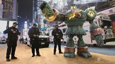 two police officers standing next to a giant robot statue in the middle of a city