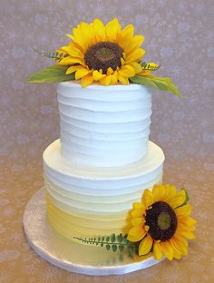 a three tiered cake with sunflowers on the top and bottom, sitting on a plate