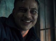 a man with green hair smiling and wearing a black hoodie in a dark room