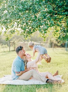 a man, woman and child sitting on a blanket under a tree