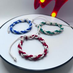 three bracelets are sitting on top of a white plate with red, white and blue cords