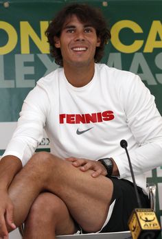 a tennis player sitting in front of a microphone with his hands on his hips and smiling