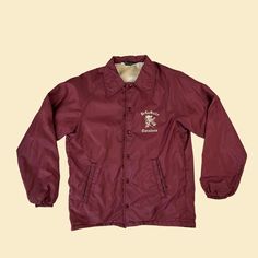 Vintage windbreaker jacket, manufactured ca. 1970s by Champion. This maroon/red snap clasp jacket features a cotton lining, long sleeves, collar, and two side pockets. The piece has a "De La Salle Cavaliers" logo on the front right (from a New Orleans high school). The jacket is the Champion "Trainer" model.   - Time Period: 1970s  - Brand: Champion ("Styled by Champion Products Inc. Rochester NY")  - Size: Small (unsure of if boys or adult; please see measurements; fits more like men's S)  - Co Brown Cotton Long Sleeve Windbreaker, Retro Burgundy Long Sleeve Outerwear, Varsity Cotton Windbreaker For Fall, Retro Long Sleeve Varsity Jacket For Outdoor, Retro Varsity Jacket For Outdoor, Fall Varsity Cotton Windbreaker, Fall Cotton Varsity Windbreaker, Retro Cotton Windbreaker For Outdoor, Vintage Long Sleeve Varsity Jacket For Outdoor