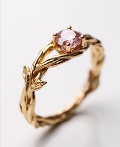 a gold ring with a pink stone in the center and leaves on it's sides