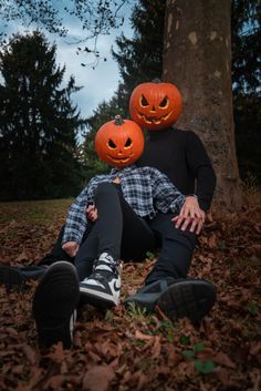 two people with pumpkin heads sitting in the leaves next to a tree and one person wearing a jack - o'- lantern mask