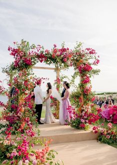 a couple getting married in front of an arch with pink and red flowers on it