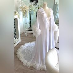 a white wedding gown on display in front of a mirror with flowers and feathers around it