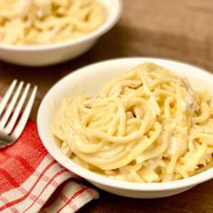 two bowls filled with pasta sitting on top of a wooden table next to a fork