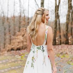 a woman in a white dress is walking through the woods with her back to the camera