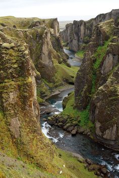 a river running through a valley surrounded by green grass and rocky mountains in the distance