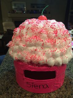 a pink cupcake with white frosting and sprinkles on top sitting on a counter