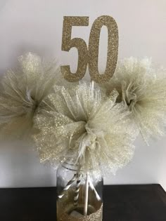 a vase filled with white flowers on top of a wooden table next to a number 50 sign