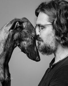 a man with long hair and glasses kissing a dog's face in black and white