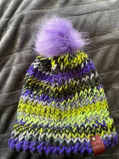 a multicolored knitted hat with a purple pom - pom on top