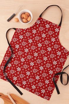 a red apron with white snowflakes on it next to eggs and utensils