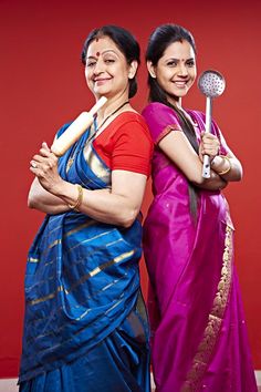 two women standing next to each other in front of a red wall holding utensils