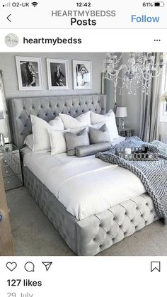 a bed with white sheets and gray pillows in a bedroom next to a mirror on the wall