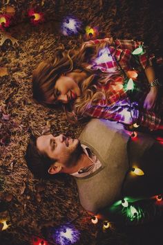 a man and woman laying on the ground with christmas lights all around them at night