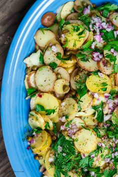 a blue plate topped with potatoes, onions and parsley next to a wooden table