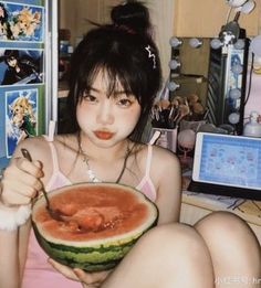 a woman holding a piece of watermelon in front of her face while sitting on the floor