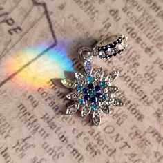 a brooch that is sitting on top of a piece of paper with a rainbow in the background