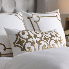 a bed with white and gold pillows on top of each other in front of a night stand