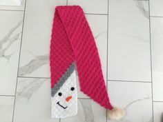 a pink knitted scarf with a snowman face on the end and a white pom - pom attached to it