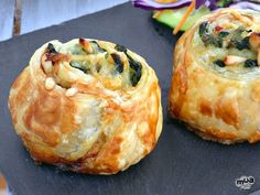 two rolls with spinach and cheese sitting on top of a cutting board next to vegetables