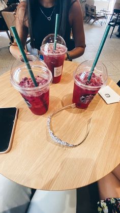 two women sitting at a table with drinks in front of them on their cell phones