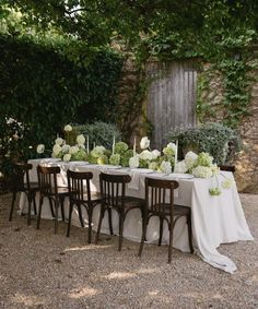 a table set up with white flowers and greenery on it for an outdoor dinner