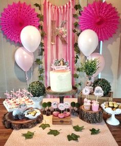 a table topped with cake and desserts next to pink decorations on top of wooden slices